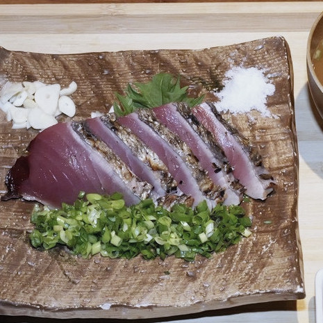 木の板に盛られた藁焼き鰹のたたきと、刻んだ葱