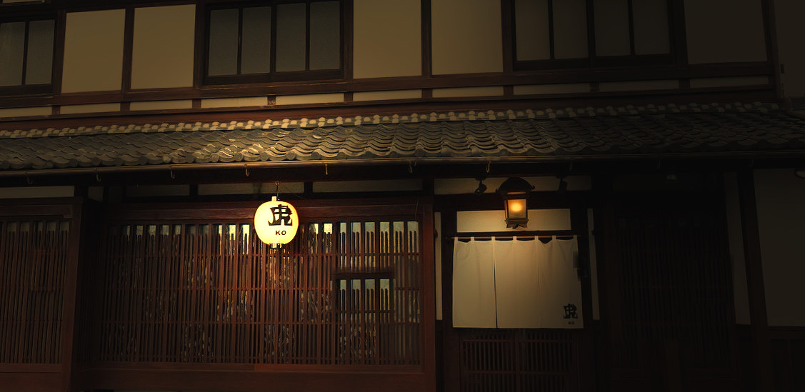 日が落ちた町屋の正面。瓦屋根の下で提灯と軒の行灯に灯がともり、白い暖簾が浮かぶ